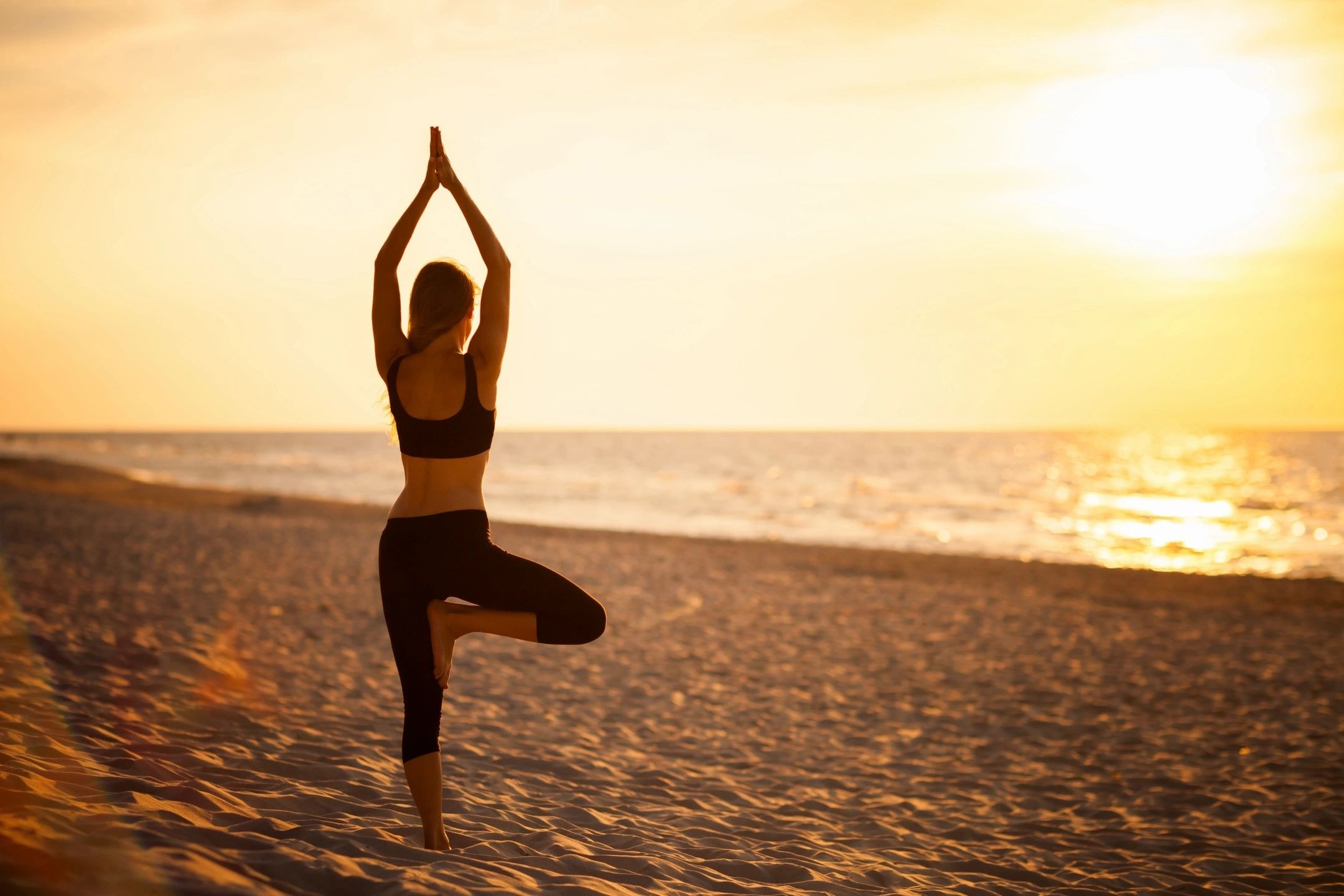 Yoga tree pose silhouette at sunset on a beach